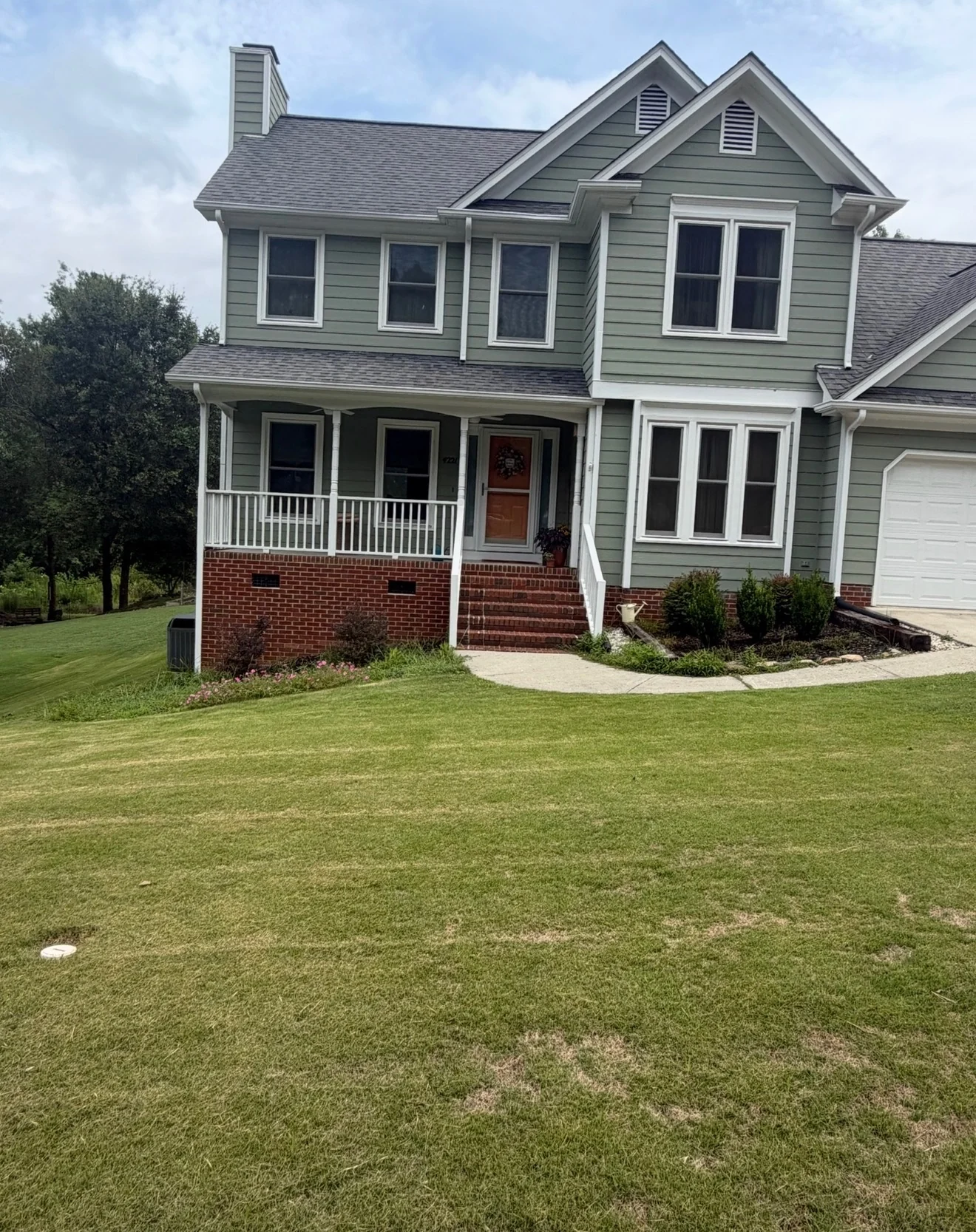 Before the North Hills retaining-wall project: a sloping lawn meets planting beds beside a brick porch and front steps.
